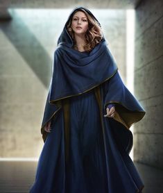 a woman in a blue cloak is walking down the street with her hands on her hips