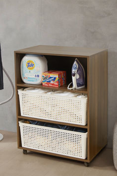 a wooden cabinet with two baskets and laundry detergents on the bottom, next to a computer monitor