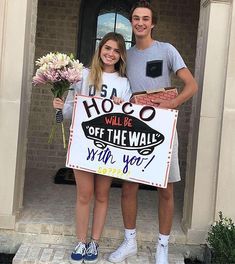 a man and woman standing in front of a door holding a sign that says hoco will be off the wall with you