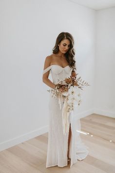 a woman wearing a white dress holding a bouquet in her hand and looking down at the floor