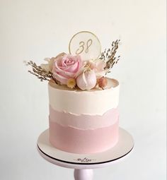 there is a pink and white cake with flowers on the top, sitting on a stand