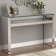 a mirrored console table with flowers and pictures on the shelf next to it in front of a mirror