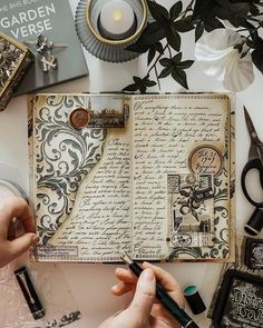 a person is writing on an open book with some scissors and other items around it