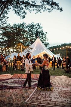 a man and woman dancing in front of a crowd at an outdoor event with string lights