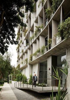 two people are walking down the sidewalk in front of a building with plants growing on it