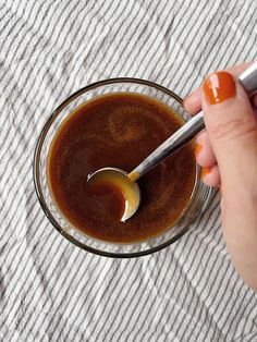 a person holding a spoon in a glass bowl filled with brown liquid on top of a white towel