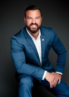 a man in a blue suit and white shirt is posing for the camera with his hands on his knees