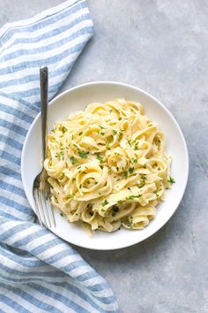 a white plate topped with pasta and parsley next to a fork on top of a blue towel