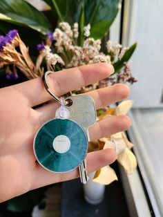 a hand holding a keychain with a disc on it and flowers in the background