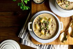 two bowls filled with soup on top of a wooden table next to silver spoons