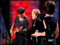 two women and a man are standing on stage with an electric guitar in front of them