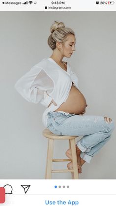 a pregnant woman sitting on top of a wooden stool with her stomach exposed and wearing ripped jeans