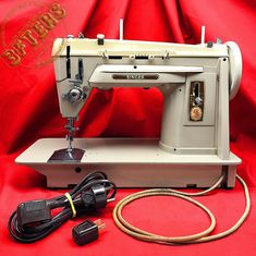 an old sewing machine sitting on top of a red cloth covered table next to a power cord