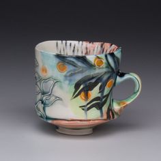 a coffee cup with oranges and leaves painted on the inside is sitting in front of a gray background