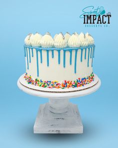 a white cake with blue icing and sprinkles on a stand against a blue background