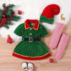 a green dress and red hat sitting on top of a wooden floor next to christmas decorations