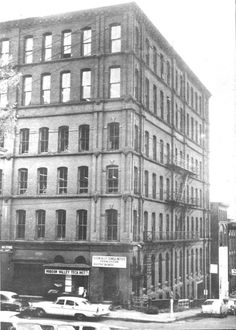 an old black and white photo of cars parked in front of a tall brick building