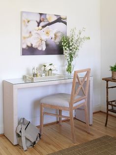 a white desk with a mirror and flowers on it next to a wooden chair in a room