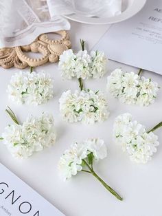 white flowers are arranged on a table next to a card and some cookies with lace