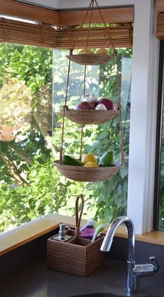 a kitchen sink under a window next to a basket with fruit on it and a faucet