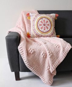 a couch with a pink blanket on top of it next to a pillow and throw