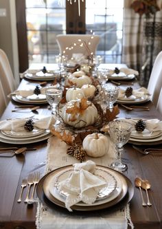 a dining room table set for thanksgiving with white pumpkins, pine cones and silverware