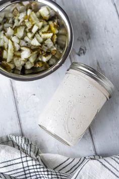 a glass jar filled with chopped vegetables next to a metal bowl on top of a white wooden table