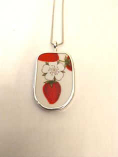 a necklace with a strawberry and flower design on the front, hanging from a silver chain