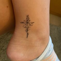 a woman's foot with a cross and flower tattoo on the bottom of her ankle