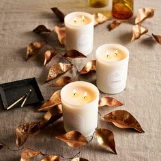 three candles sitting on top of a table covered in leaves