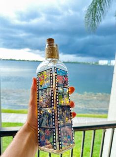 a person holding up a bottle with pictures on it in front of a balcony overlooking the ocean