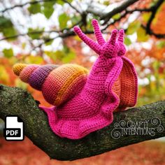 two crocheted hats sitting on top of a tree branch in front of leaves