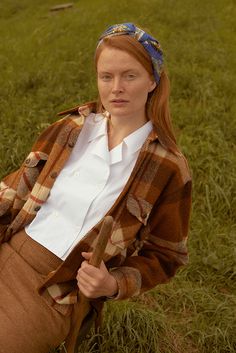 a woman sitting in the grass wearing a plaid jacket