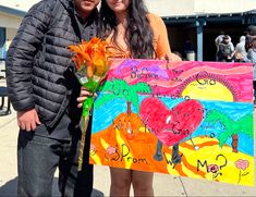 a man and woman standing next to each other holding a sign with flowers on it