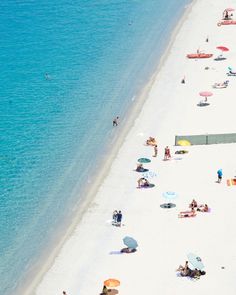 many people are on the beach with umbrellas and chairs near the water's edge