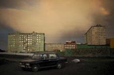 an old car is parked in the middle of a parking lot with apartment buildings in the background