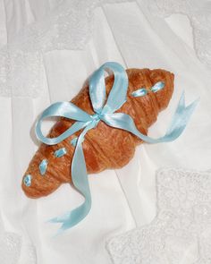 a croissant wrapped in blue ribbon and sitting on a white sheet with lace