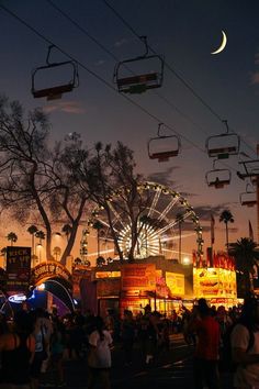 the ferris wheel is lit up at night in front of an amusement park with many people