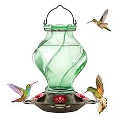 two hummingbirds are flying near a green bird feeder that is hanging from the ceiling