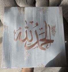 a person holding up a painting with arabic writing on it's side, in front of a couch