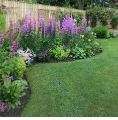 a garden filled with lots of flowers next to a wooden fence and green grass covered yard