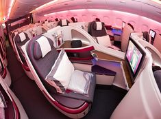 the inside of an airplane with many seats and televisions on each side of it