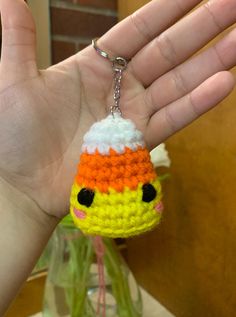 a hand holding a small crocheted keychain with an orange and white hat on it