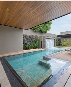 an outdoor swimming pool with waterfall and lounge chairs in the foreground, surrounded by greenery