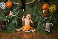 a baby sitting in front of a cake surrounded by jungle decorations