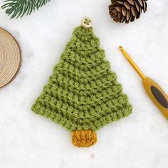 a crocheted christmas tree ornament next to a pine cone and knitting needles