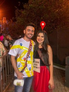 a man and woman standing next to each other on a sidewalk at night with people in the background