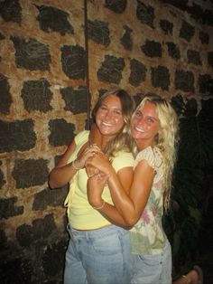 two women hugging each other in front of a brick wall