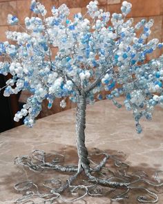 a wire tree with blue and white beads on it sitting on a marble table top