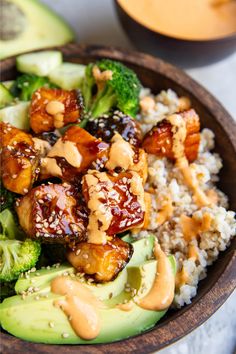 a wooden bowl filled with rice, broccoli and chicken covered in peanut sauce